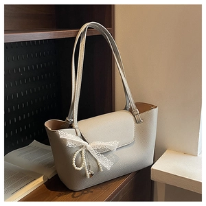 Detail of beige tote bag featuring lace bow, pearl chain, and heart pendant decoration