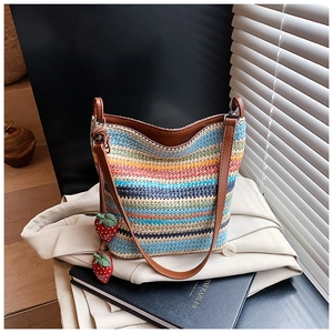 Detail of colorful woven bucket bag featuring strawberry charms on a beige blazer background