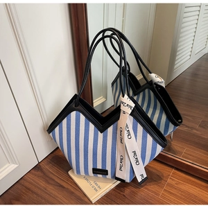 Detail of blue striped canvas tote bag with black leather trim and decorative ribbon