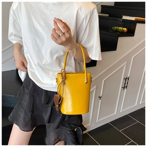 Detail of yellow bucket bag with brown heart charm held by a model on a staircase