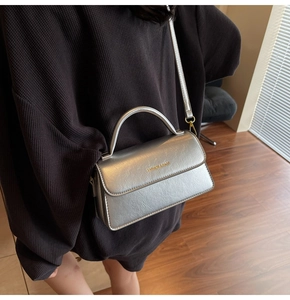 Silver PU leather crossbody bag with top handle and gold logo detail worn by model