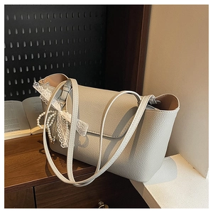 Detailed shot of beige lychee leather tote with white lace bow and pearl charm accents