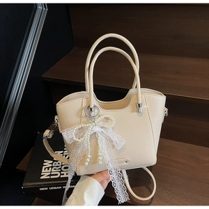 Détail du sac crème avec texture litchi, nœud en dentelle et breloques en perles