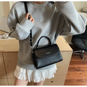 Detail of black lychee grain leather handbag with adjustable strap and brand logo