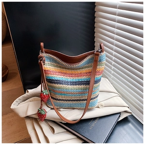 Close-up of a colorful woven bucket bag with leather trim and strawberry charms
