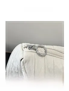 Close-up of the smooth silver circular zipper pull on a beige quilted dumpling shoulder bag