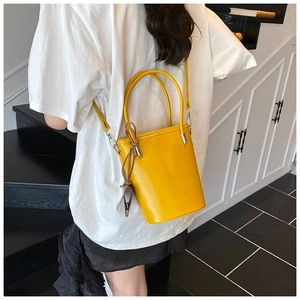 Detail of bright yellow leather bucket bag with cylindrical handles and knot ornament