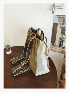 Detail of a two-tone drawstring backpack in mustard and green on a wooden table