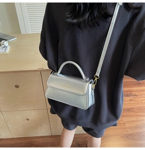 Silver metallic PU leather crossbody bag worn over a dark coat in a home setting