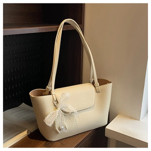 Close-up of beige lychee grain tote bag with lace bow and pearl charm on a shelf