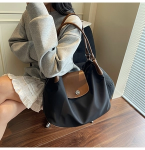 Close-up of black tote bag featuring brown leather flap and silver metal button detail