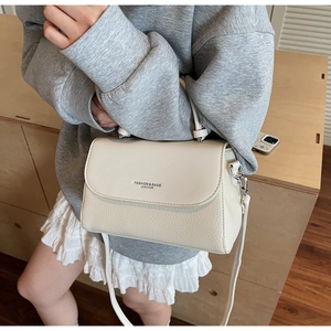 Detail view of cream leather handbag showing fine pebble grain texture and metal hardware