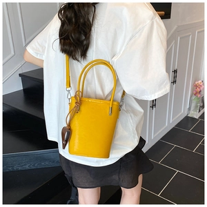 Detailed view of yellow bucket bag with double handles and heart-shaped pendant