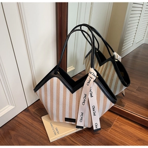Detail of striped canvas tote with black leather trim and decorative branded ribbon