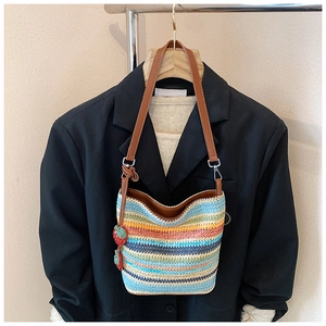 Close-up of rainbow striped straw shoulder bag with strawberry charm and leather strap