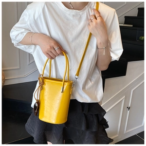 Detail view of bright yellow bucket bag with double handles and brown leather tag charm