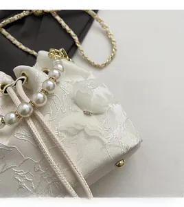 Close-up of white bucket bag with floral embroidery, pearl handle, and butterfly accents