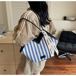 Detail of striped canvas tote bag with leather straps and decorative ribbon on side