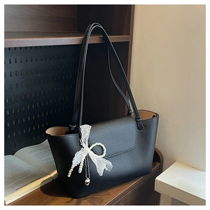 Detail of black tote bag with lace bow, pearl charms and heart pendant on wood shelf