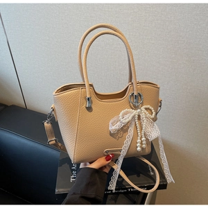 Gros plan du sac en cuir litchi beige avec nœud en dentelle blanche et breloque perle