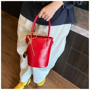 Detail of red leather bucket bag with brown decorative bow and mini pouch attachment