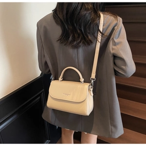 Rear view of a model wearing the beige pebbled leather shoulder bag in an indoor setting