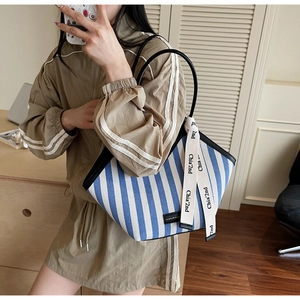 Detail of blue and white striped canvas tote with black handle and decorative ribbon detail