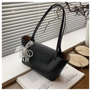 Detail of black pebble leather tote bag with elegant white lace and pearl bow charm