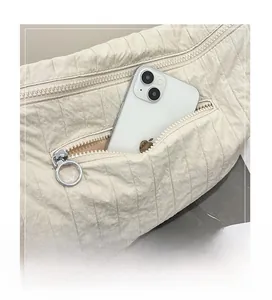Detail of the rear zipper pocket on ivory quilted crossbody bag holding a large smartphone