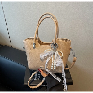 Détail du sac cabas beige grainé avec nœud en dentelle et perles sur un livre