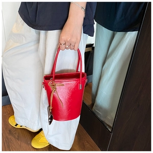 Detail of red patent leather bucket bag featuring a sleek finish and top handle design