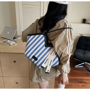Detail of blue striped canvas tote bag with leather trim and decorative ribbons
