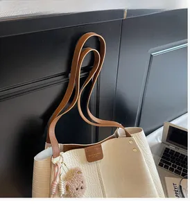 Detail of cream faux crocodile leather tote bag featuring a cute brown plush bear charm