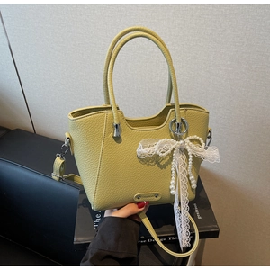 Détail du sac cabas en cuir vert avec un nœud décoratif en dentelle et perles blanches