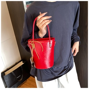 Detail of a bright red bucket bag with woven drawstring knot and polished metal hardware