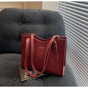 Detail of vintage red leather tote with gold logo on a gray corduroy surface
