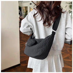 Detail of black pleated crossbody bag with matching round coin purse on back of female model