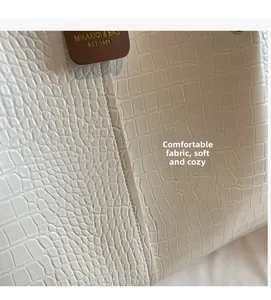 Detail of cream crocodile texture fabric and brown leather brand tag on a tote bag
