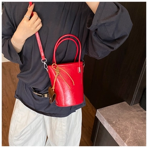 Detail of red leather bucket bag with top handles, heart charm, and slim crossbody strap