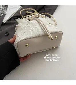 Detail of protective gold-tone studs on the base of a white lace pearl bucket bag