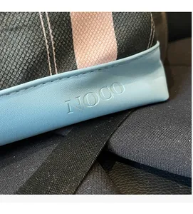 Close-up of the NOCO logo embossed on light blue leather with woven tweed texture