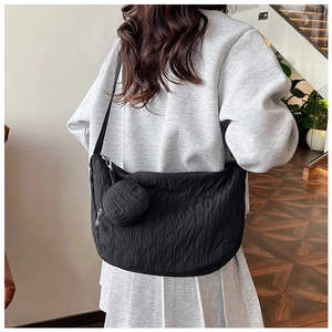 Detail view of black dumpling crossbody bag with pleated texture and round pouch charm