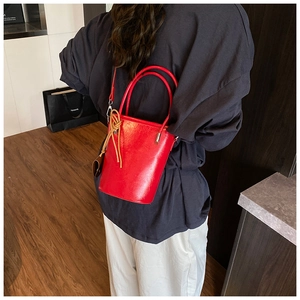 Model view of red polished leather bucket bag with decorative woven pendant