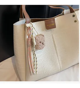 Detail of crocodile embossed tote bag with woven pendant and cute bear charm