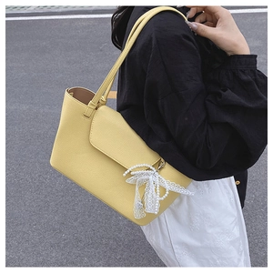 Detail of yellow pebbled leather shoulder bag featuring a lace and pearl bow charm