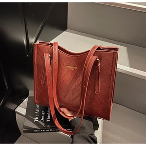 Macro detail of dark red leather tote bag showing wrinkled texture and gold lettering