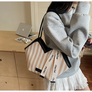 Close-up of striped canvas tote bag with leather trim and shoulder strap on model