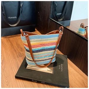 Detail of colorful woven straw bucket bag with brown leather strap and silver metal hooks