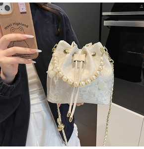 Detail of white lace bucket bag featuring a pearl handle and delicate floral embroidery