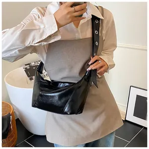 Détail du sac croissant noir brillant avec large bandoulière et œillets en métal